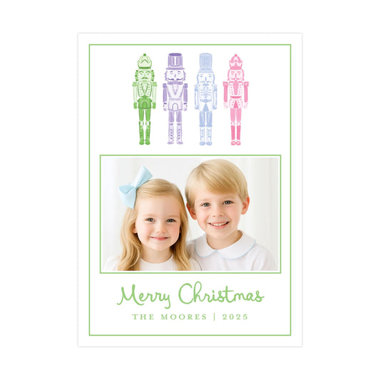 A Christmas card featuring two children, a girl and a boy, smiling together in front of a row of colorful nutcracker figures.