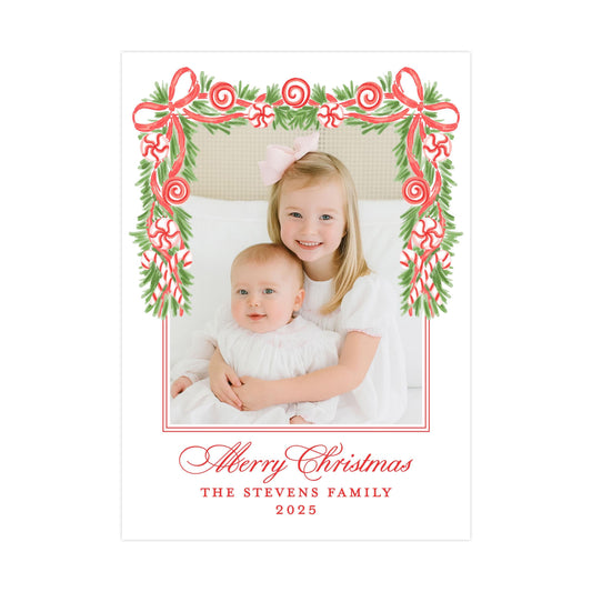 A young girl and a baby are sitting together in a frame with a festive Christmas wreath design. The text at the bottom of the image reads "Merry Christmas THE STEVENS FAMILY 2015".