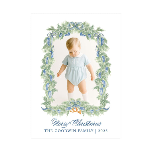 A baby dressed in a light blue outfit is standing in a wreath-like frame with green leaves and blue ribbons, surrounded by a festive holiday design. The image is a collage of multiple smaller images, and the text at the bottom reads "Merry Christmas THE GOODWIN FAMILY 2025".