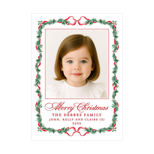 A framed photograph of a young girl with a Christmas wreath border. The text below the photo reads "Merry Christmas THE DERBES FAMILY JOHN, KELLY AND CLAIRE (3) 2023".