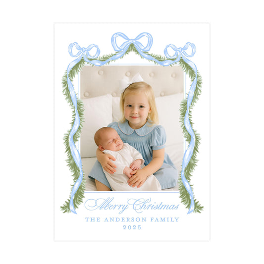 A young girl in a blue dress is holding a sleeping baby in her arms, with a festive Christmas-themed frame surrounding them. The text at the bottom of the image reads "Merry Christmas THE ANDERSON FAMILY 2015".