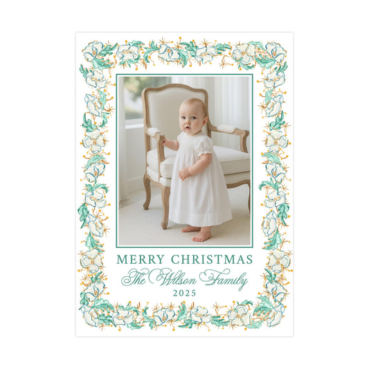 A baby girl in a white dress is standing in front of a chair, with a floral border framing the image. The text "Merry Christmas The Wilson Family" is displayed around the border, indicating the holiday season and the family's name.