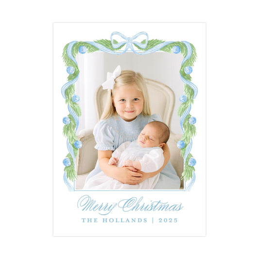 A young girl in a blue dress is holding a sleeping baby in her arms, with a decorative frame around them. The text at the bottom of the image reads "Merry Christmas THE HOLLANS | 2025".