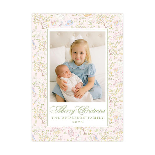 A young girl in a blue dress is holding a sleeping baby in her arms, with a floral pattern surrounding them. The text at the bottom of the image reads "Merry Christmas THE ANDERSON FAMILY 2015".