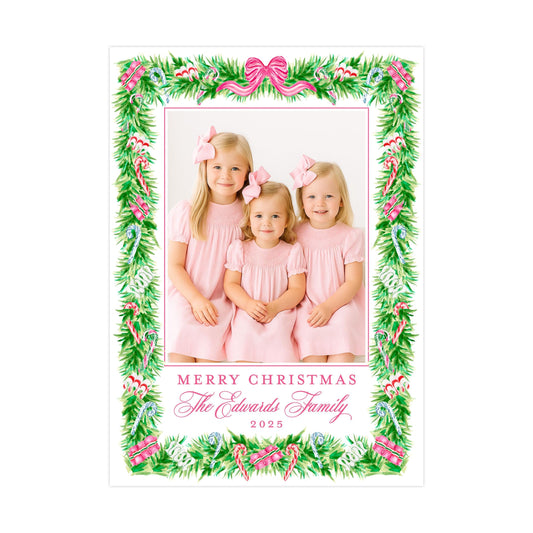 A family portrait of three young girls in pink dresses, surrounded by a festive Christmas wreath frame.