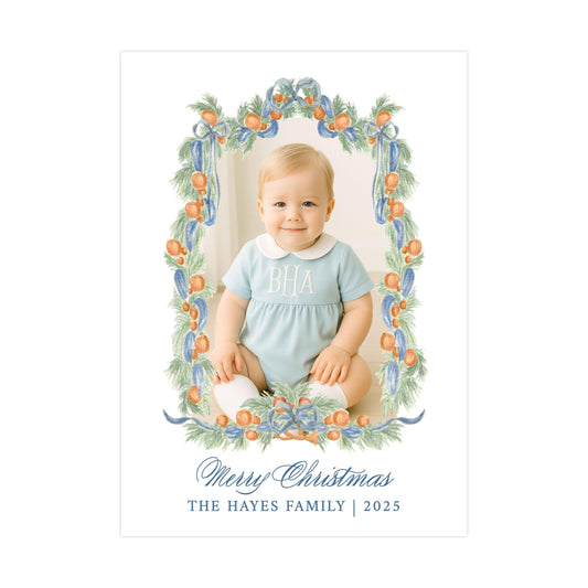 A smiling baby wearing a blue outfit with the initials "BA" on it, sitting in a decorative frame with a wreath of orange and green leaves surrounding it. The text below the image reads "Merry Christmas" and "THE HAYES FAMILY | 2025".