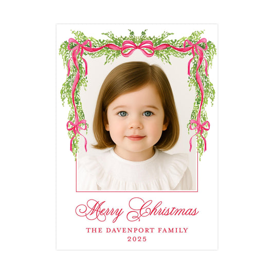 A young girl with brown hair and blue eyes is smiling at the camera, framed by a decorative border of pink ribbons and greenery. The text below the image reads "Merry Christmas" and "THE DAVENPORT FAMILY" along with the year "2025".