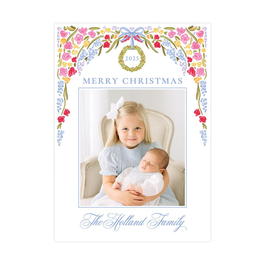 A young girl is holding a sleeping baby in her arms, with a floral wreath and the year "2023" displayed above them. The text "Merry Christmas" is written at the top, and "The Holland Family" is written at the bottom.