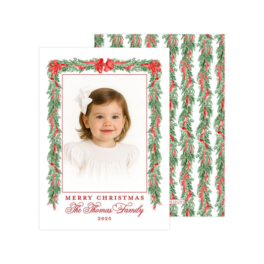 A framed photograph of a young girl with a bow in her hair, surrounded by a festive wreath of greenery and red berries. The text on the card reads &quot;Merry Christmas The Thomas Family, 2015&quot;.