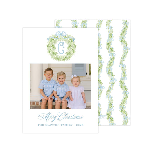 A family photo of three children, two boys and a girl, sitting on a porch with a wreath above them. The photo is framed with a border and the text &quot;Merry Christmas&quot; and &quot;The Clayton Family | 2025&quot; is displayed below the photo.