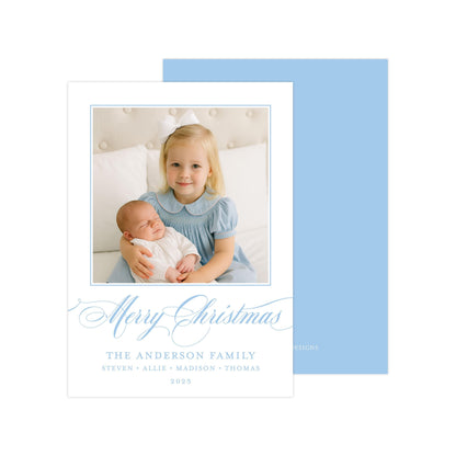 A young girl in a blue dress is holding a sleeping baby in her arms, with a "Merry Christmas" message and the name "The Anderson Family" written below.