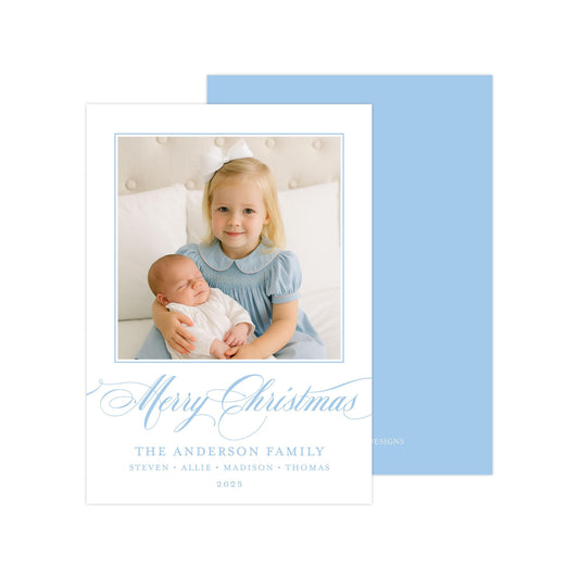 A young girl in a blue dress is holding a sleeping baby in her arms, with a "Merry Christmas" message and the name "The Anderson Family" written below.