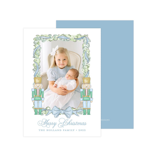 A young girl is holding a baby in a photo frame with nutcracker figures, surrounded by a decorative border. The text on the card reads &quot;Merry Christmas&quot; and &quot;The Holland Family - 2025&quot;.