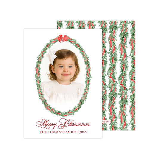 A Christmas card featuring a young girl with a bow in her hair, surrounded by a wreath of greenery and red ribbons. The card has a personalized message and a year printed on it.