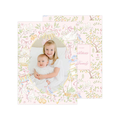 A young girl is holding a baby in a pink and white floral frame, with a pattern of birds, flowers, and leaves surrounding them.