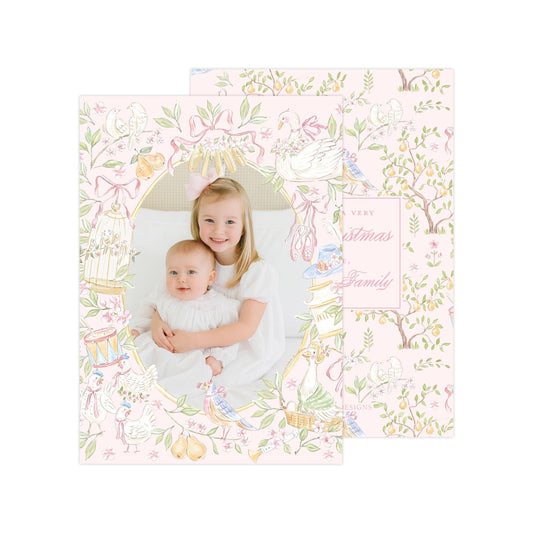 A young girl is holding a baby in a pink and white floral frame, with a pattern of birds, flowers, and leaves surrounding them.