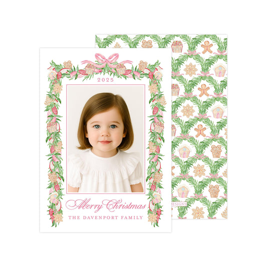 A personalized Christmas card featuring a young girl in a white dress, with a floral border and a photo of her. The card has a festive design with a pattern of gingerbread cookies and pine branches.