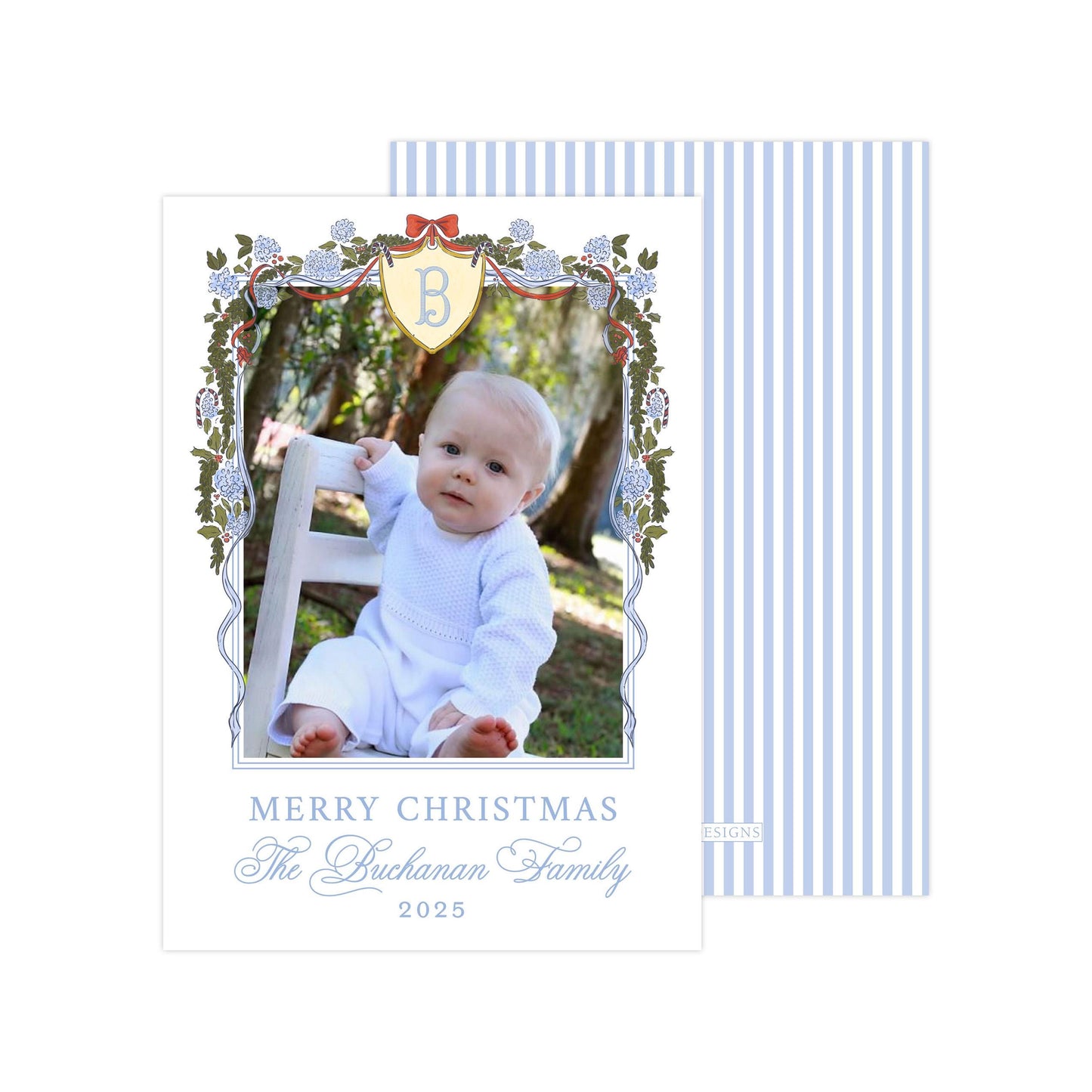 A baby sitting in a chair, surrounded by a decorative border with a blue and white striped pattern. The baby is wearing a white outfit. The image is framed with a border that includes a floral design and a shield-shaped emblem. The text at the bottom of the image reads "MERRY CHRISTMAS The Buchanan Family 2015".