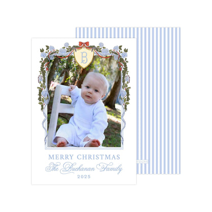 A baby sitting in a chair, surrounded by a decorative border with a blue and white striped pattern. The baby is wearing a white outfit. The image is framed with a border that includes a floral design and a shield-shaped emblem. The text at the bottom of the image reads "MERRY CHRISTMAS The Buchanan Family 2015".