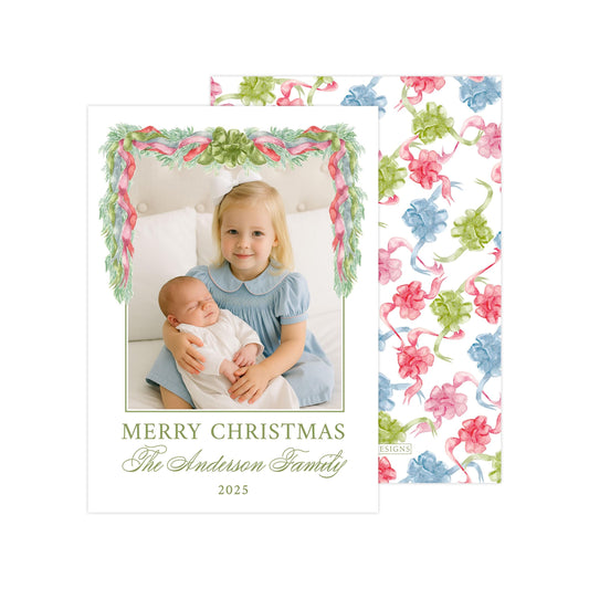 A young girl in a blue dress is holding a baby in her arms, with a floral border framing the image. The text "MERRY CHRISTMAS The Anderson Family 2020" is displayed below the image.