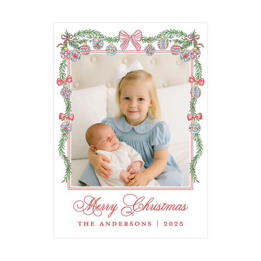 A young girl in a blue dress is holding a sleeping baby in her arms, with a festive Christmas-themed frame surrounding them. The text &quot;Merry Christmas&quot; and &quot;THE ANDERSons | 2025&quot; is visible, indicating the holiday season and the name of the family.