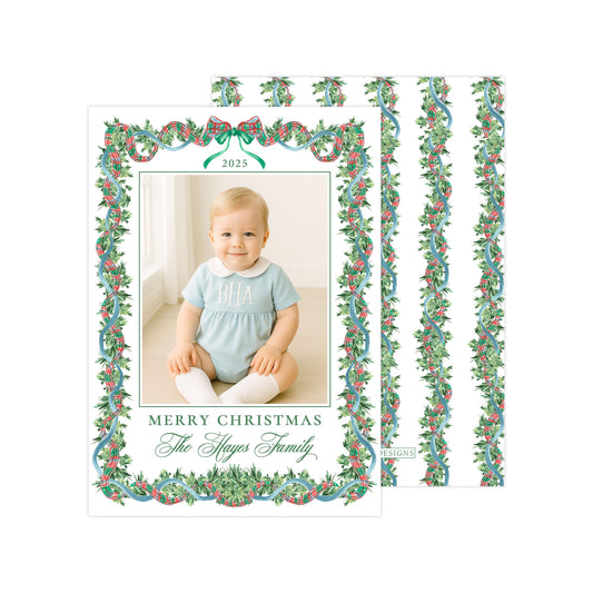A photo of a smiling baby girl wearing a blue onesie, framed within a decorative border with a holly and mistletoe pattern. The text "Merry Christmas The Hayes Family" is displayed around the photo.