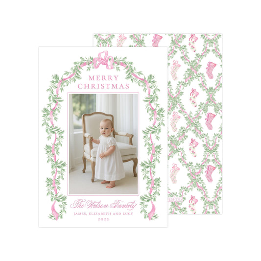 The image is a Christmas card featuring a baby girl in a white dress, standing in front of a chair with a floral border. The card has a pink and green color scheme and includes a photo of the baby girl.