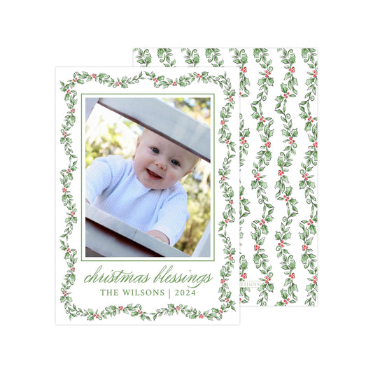A photo of a smiling baby wearing a white outfit, framed within a decorative border with a holly leaf pattern. The text &quot; christmas blessings THE WILSONS | 2024&quot; is displayed below the photo.