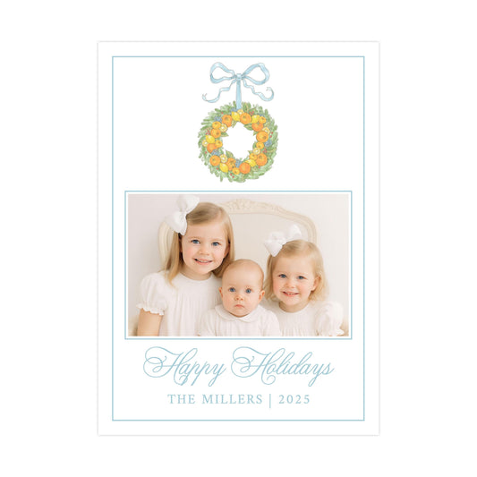 A family portrait of three young girls, likely sisters, with a wreath of oranges above them. The text below the image reads "Happy Holidays THE MILLERS | 2025".