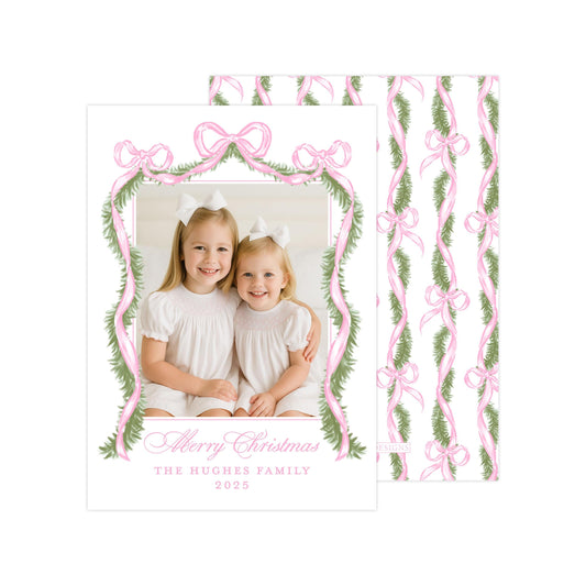 A Christmas card featuring two young girls in white dresses, smiling and posing together. The card has a pink and green floral border and a bow design, and includes a message that reads &quot;Merry Christmas The HUGGES FAMILY 2015&quot;.