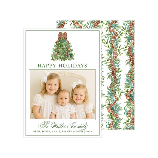 A holiday card featuring three young girls in white dresses, with a Christmas tree and ribbon design. The card has a festive and cheerful design with the text &quot;Happy Holidays&quot; and &quot;The Miller Family&quot; written on it.