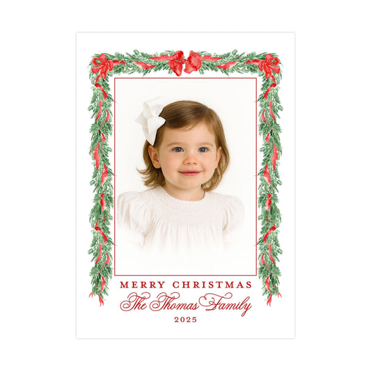 A young girl with a white bow in her hair is the central focus of the image, framed within a decorative border of red and green leaves and flowers. The text &quot;Merry Christmas The Thomas Family 2020&quot; is displayed around the border, indicating the holiday season and the family&#39;s name.