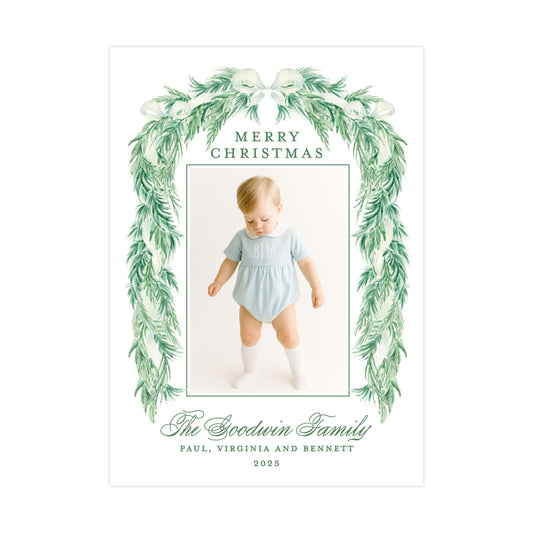 The image is a Christmas card featuring a baby wearing a light blue outfit, surrounded by a green wreath. The card has a message that reads "Merry Christmas" and includes the names "Paul, Virginia and Bennett" along with the year "2025".