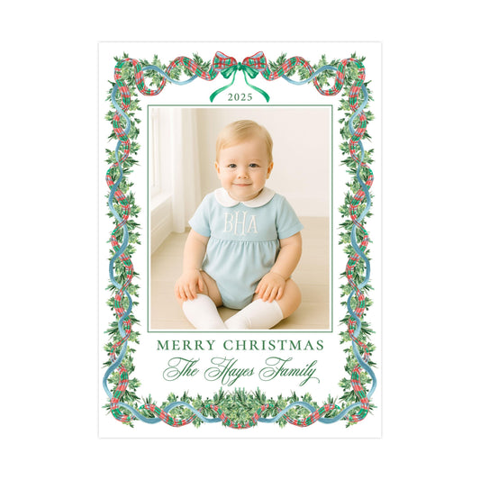 A smiling baby wearing a light blue outfit with the initials "BA" on it, sitting on a wooden floor. The image is framed by a decorative border with a Christmas wreath pattern. The text "Merry Christmas The Skyes Family" is displayed around the border.