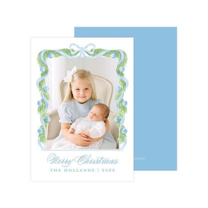 A young girl is holding a sleeping baby in her arms, with a blue and white floral frame surrounding them. The text &quot;Merry Christmas&quot; and &quot;THE HOLLANDS | 2025&quot; is displayed below the image.
