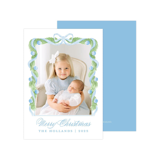 A young girl is holding a sleeping baby in her arms, with a blue and white floral frame surrounding them. The text &quot;Merry Christmas&quot; and &quot;THE HOLLANDS | 2025&quot; is displayed below the image.