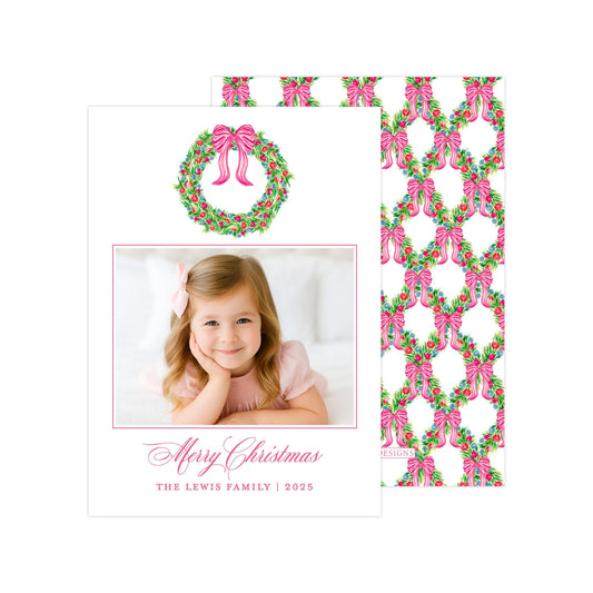 A Christmas card featuring a young girl with a bow in her hair, smiling at the camera, and a wreath with pink bows above her.