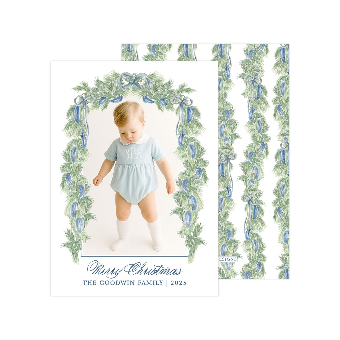 A photo of a baby wearing a light blue onesie, standing in front of a floral archway with a "Merry Christmas" greeting.