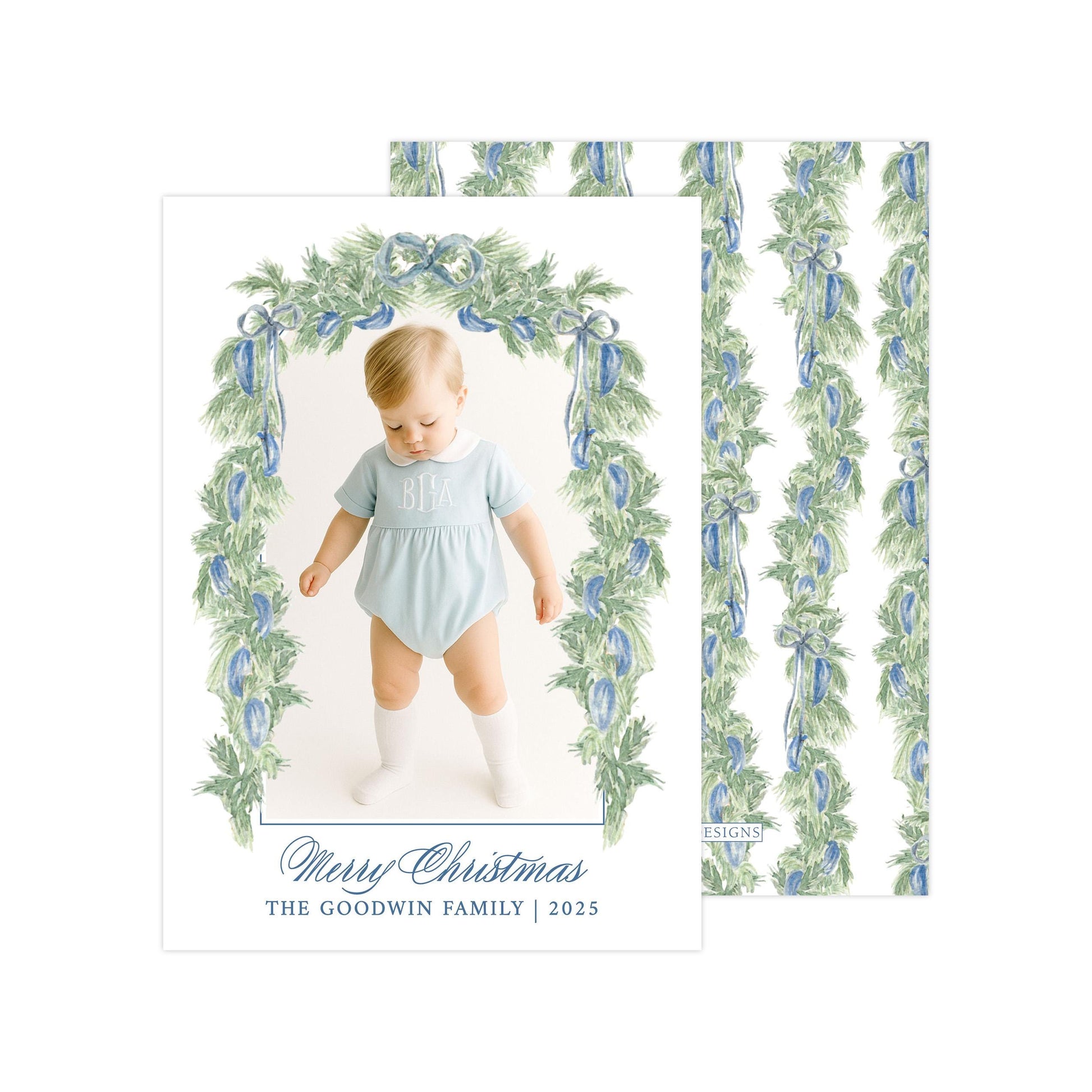 A photo of a baby wearing a light blue onesie, standing in front of a floral archway with a "Merry Christmas" greeting.