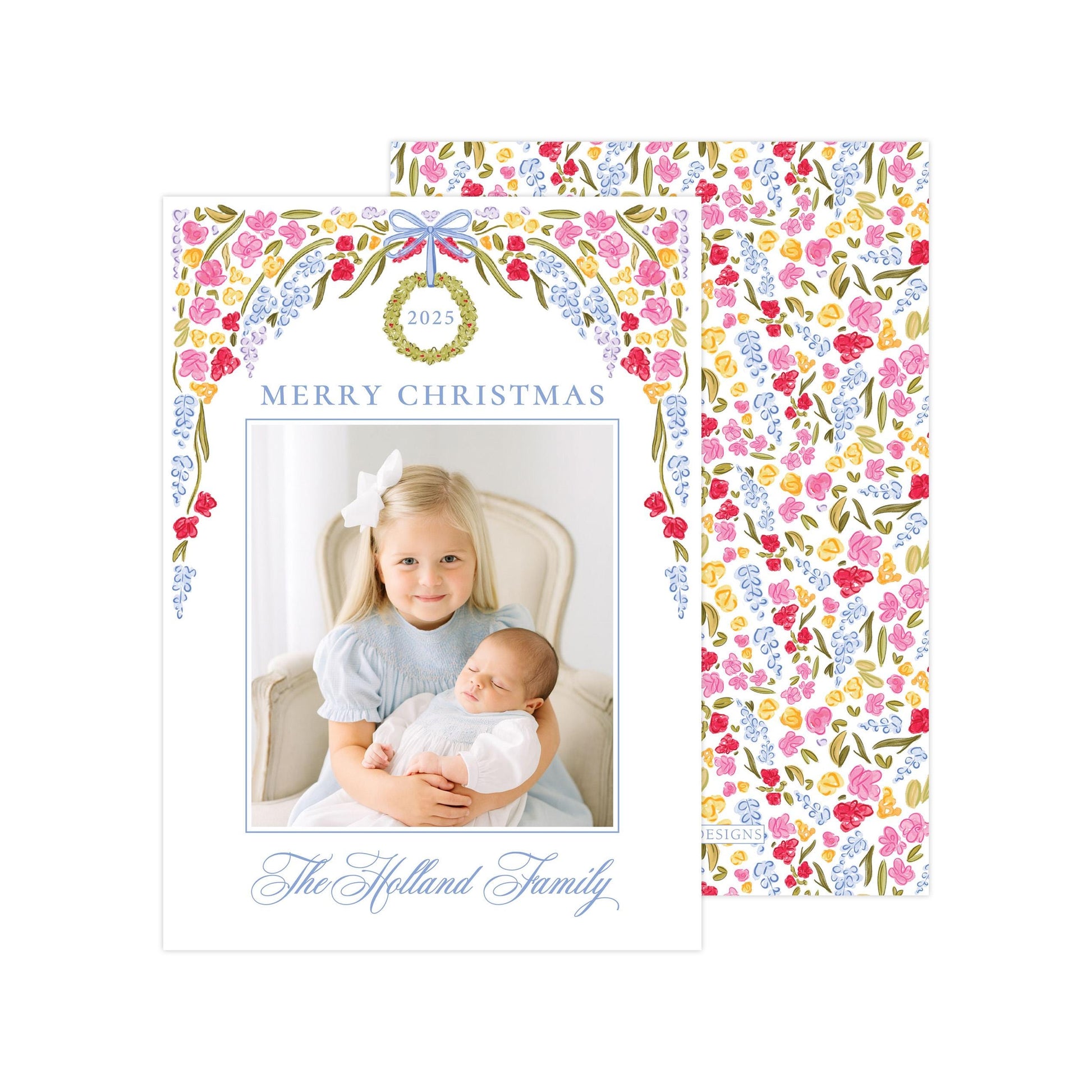 A Christmas card featuring a young girl holding a sleeping baby, with a floral wreath design above the photo.