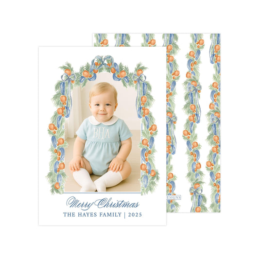 A photo of a smiling baby girl wearing a blue outfit, sitting in a frame with a floral border. The text below the photo reads "Merry Christmas THE HAYES FAMILY | 2025".