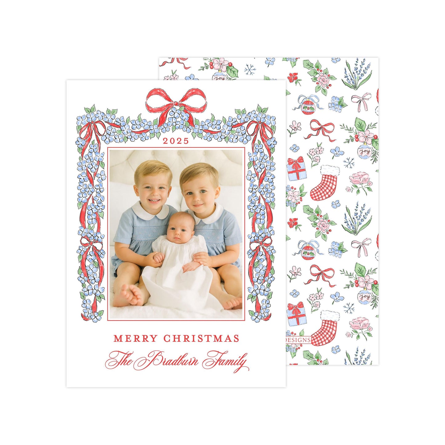 A Christmas card featuring two young boys sitting on a bed, with a baby between them, and a floral border around the photo. The card has a festive design with red and white ribbons and flowers, and the text &quot;Merry Christmas The Bradbury Family&quot; is displayed.