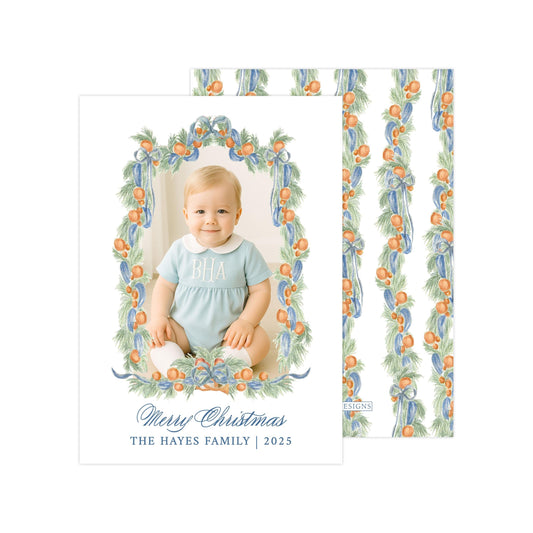 A photo of a smiling baby wearing a blue outfit, surrounded by a wreath of orange and green leaves. The text below the image reads "Merry Christmas THE HAYES FAMILY | 2025".