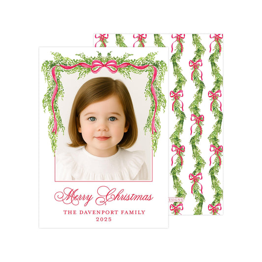 A young girl with a warm smile is featured in a festive Christmas card, surrounded by a wreath of greenery and pink ribbons. The card is addressed to "The Davenport Family" and includes a personalized photo of the girl.