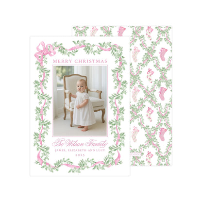 The image is a Christmas card featuring a baby girl in a white dress, surrounded by a pink and green floral border. The card has a festive design with a pattern of pink and green leaves and stockings. The text on the card reads &quot;Merry Christmas&quot; and &quot;The Wilson Family&quot;, along with the names &quot;James, Elizabeth and Lucie&quot; and the year &quot;2023&quot;.