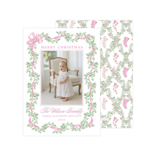 The image is a Christmas card featuring a baby girl in a white dress, surrounded by a pink and green floral border. The card has a festive design with a pattern of pink and green leaves and stockings. The text on the card reads &quot;Merry Christmas&quot; and &quot;The Wilson Family&quot;, along with the names &quot;James, Elizabeth and Lucie&quot; and the year &quot;2023&quot;.