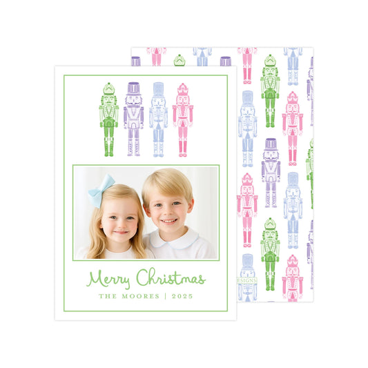 A Christmas card featuring two children, a girl and a boy, smiling together in front of a repeating pattern of nutcracker figures in various colors.